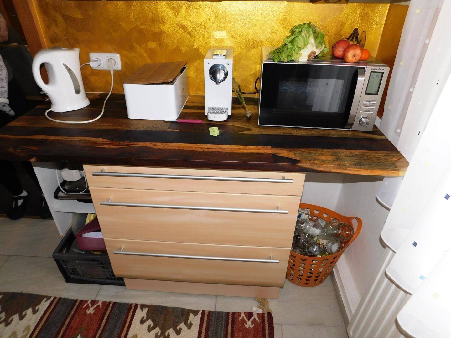 Küchenarbeitsplatte aus Holz mit Mikrowelle, Wasserkocher und Kaffeemaschine, praktisch eingerichtet.