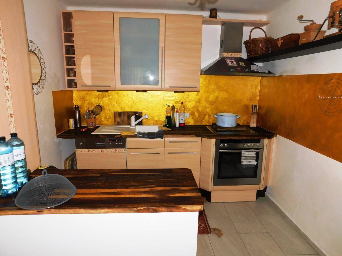 Funktionale Küche mit Spülbecken, Kochfeld und Stauraum in hellen Holzfronten, mit goldener Akzentwand.