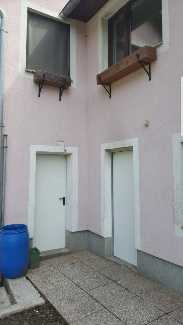 Außenansicht einer Gebäudeecke mit zwei Türen und Fenstern, rosa verputzt und schlicht gestaltet.