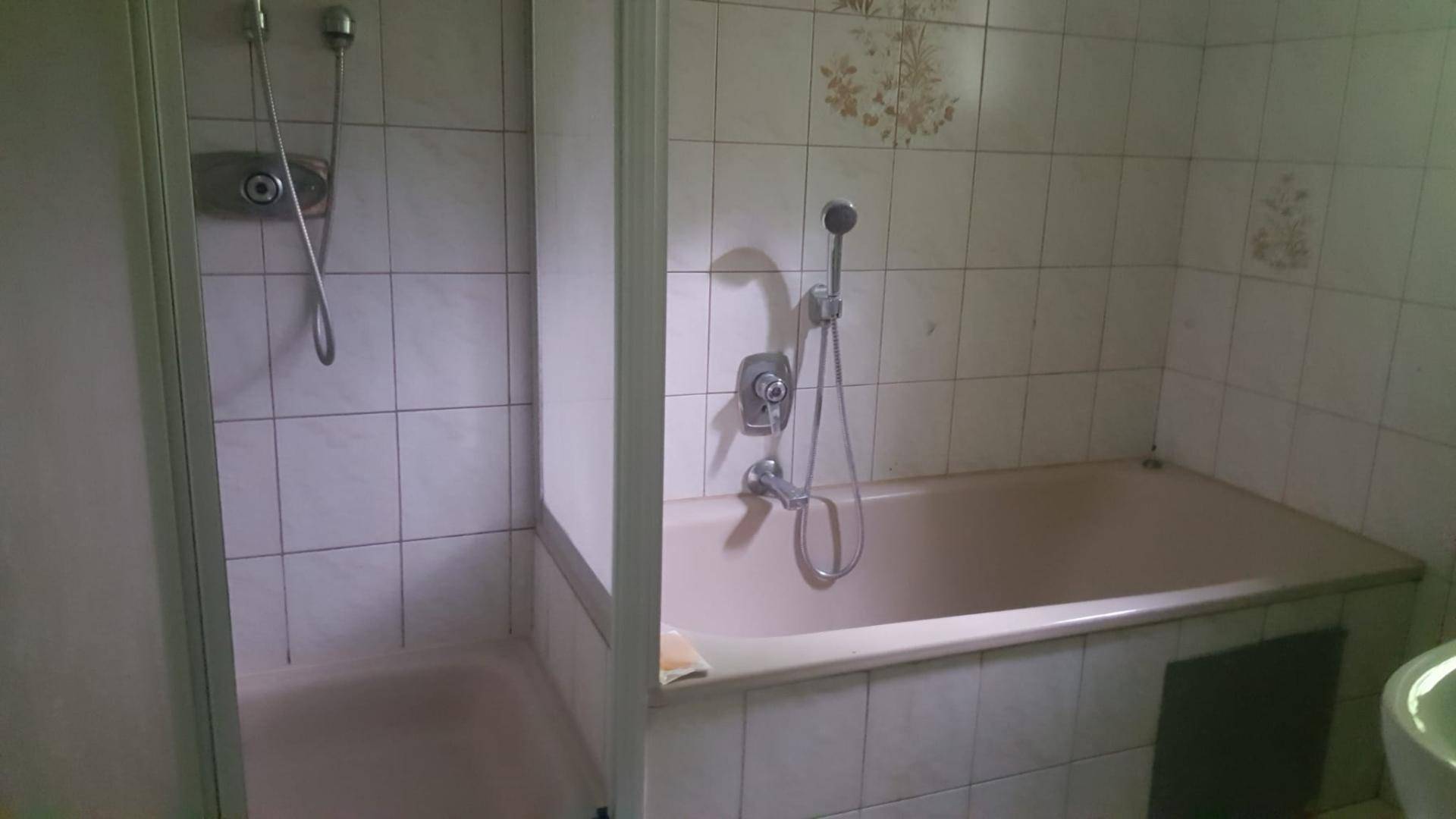Badezimmer mit Badewanne und separatem Duschbereich, gefliest in einem hellen Farbton.