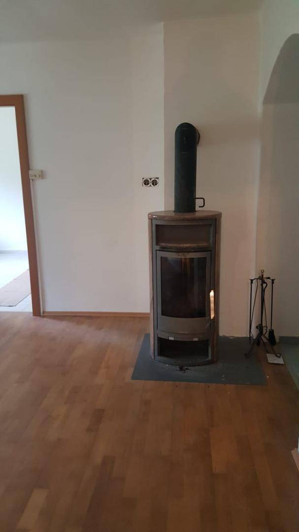 Leerer Raum mit Holzboden und einem freistehenden Holzofen als Wärmequelle, schlicht gehalten.