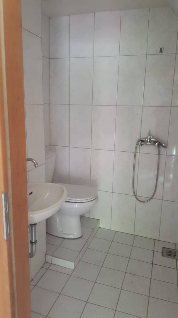 Kleines Badezimmer mit WC, Waschbecken und Duschvorrichtung, komplett mit weißen Fliesen ausgestattet.
