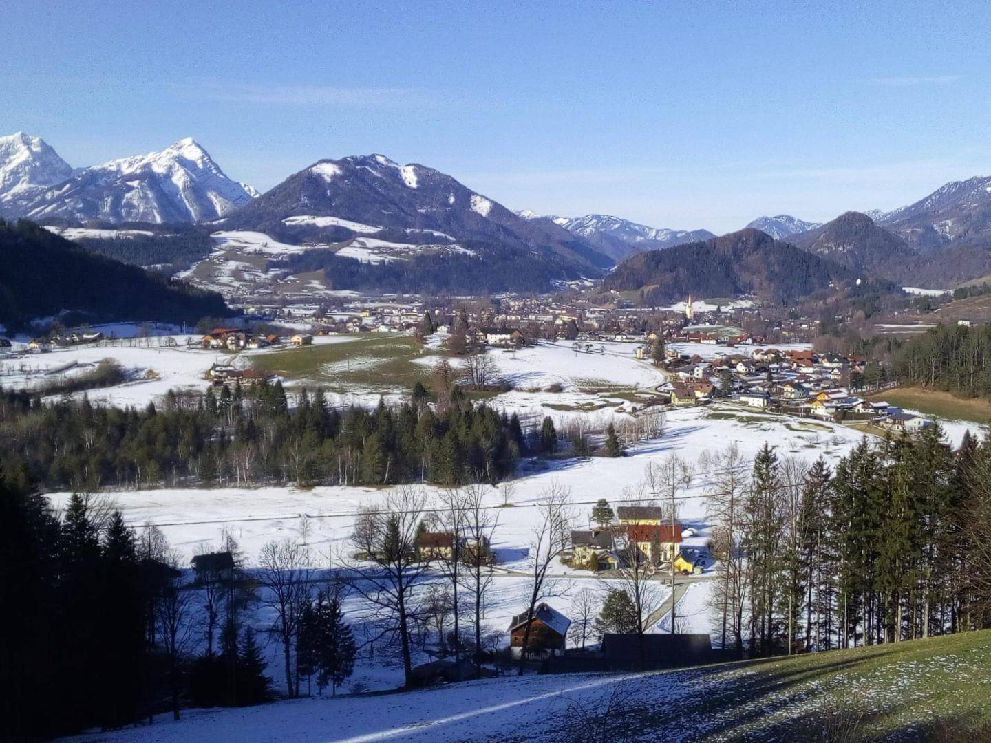 Winterliche Berglandschaft mit schneebedeckten Gipfeln und einem verschneiten Dorf im Tal.