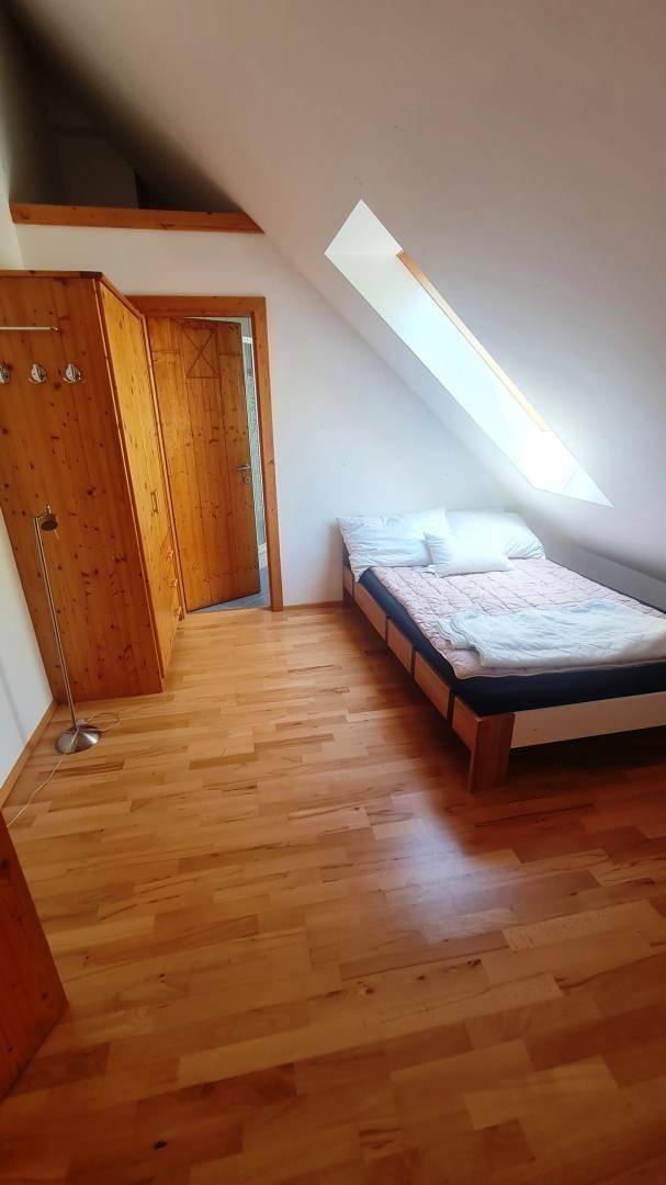 Gemütliches Schlafzimmer im Dachgeschoss mit Holzboden, Dachfenster und schrägen Wänden.
