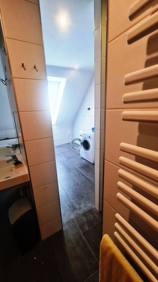Badezimmer mit Waschmaschine, Dachfenster und Fliesenboden, das viel Tageslicht bietet.