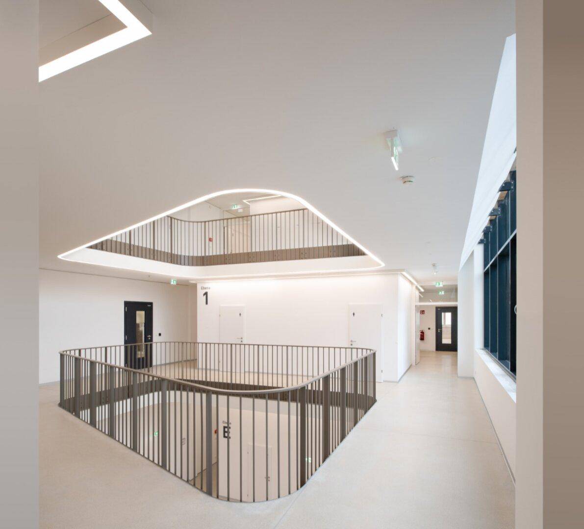 Helles, modernes Atrium mit geschwungenen Balustraden und indirekter Beleuchtung, das verschiedene Etagen verbindet.