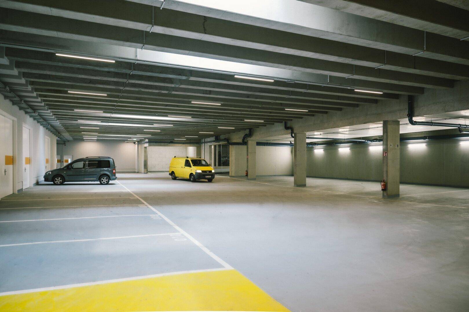 Geräumige Tiefgarage mit Betonpfeilern, hellen Leuchten und markierten Parkplätzen für Fahrzeuge.