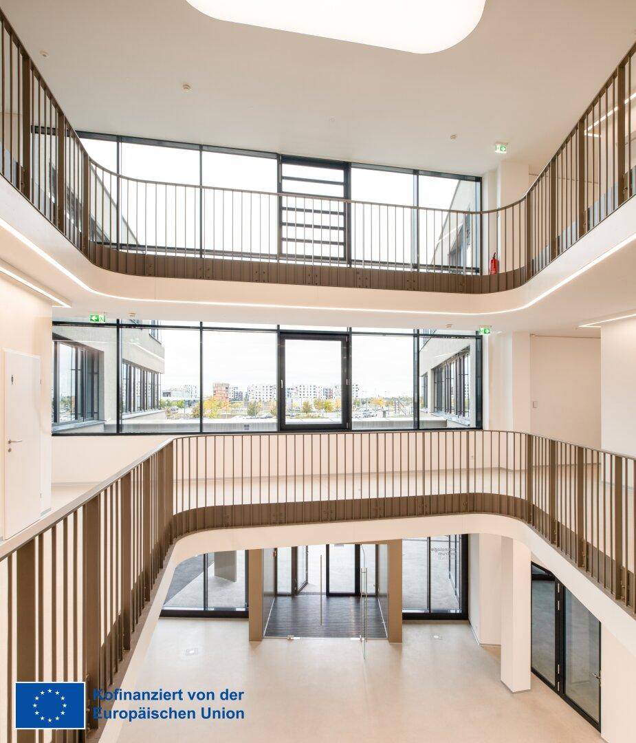 Modernes Atrium mit mehreren Ebenen, eleganten Geländern und großen Glasflächen, die viel Licht hereinlassen.