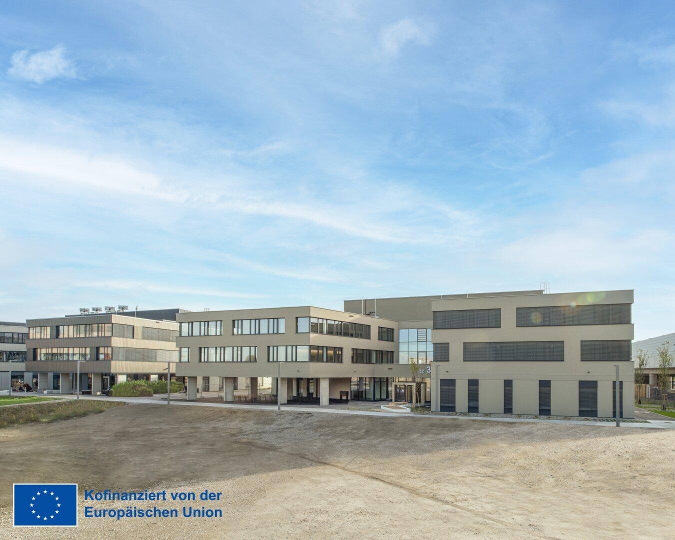 Panoramablick auf einen modernen Bürogebäudekomplex mit beiger Fassade und großen Fensterflächen.