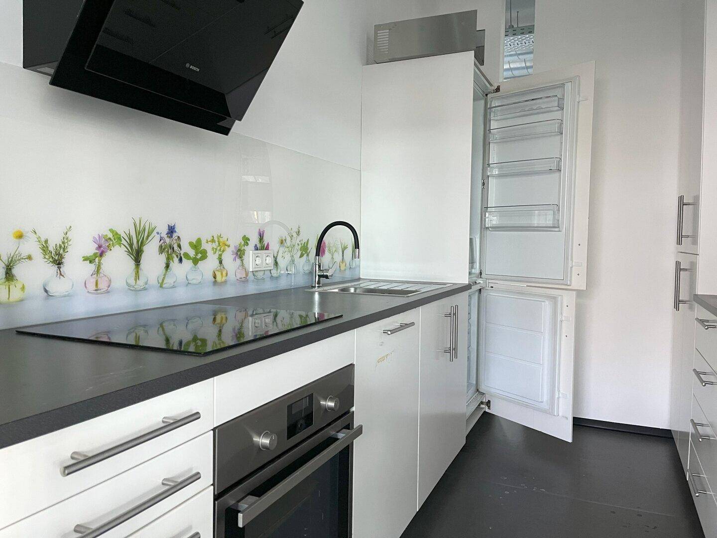 Moderne Einbauküche mit weißen Schränken, Induktionskochfeld und integriertem Kühlschrank.