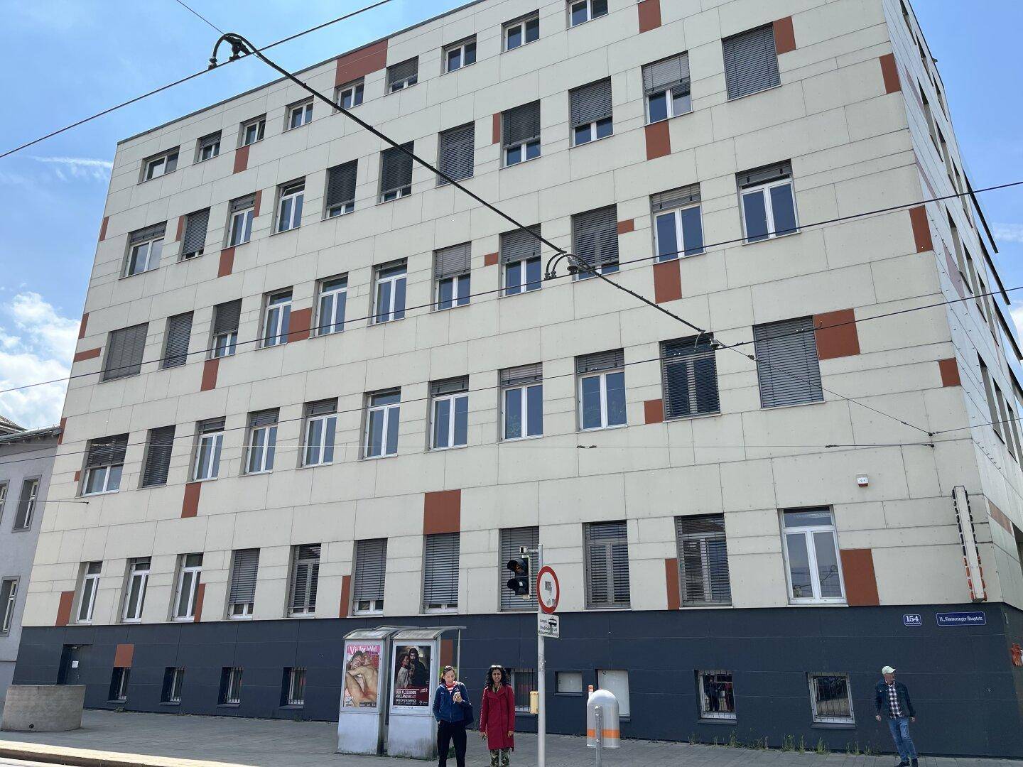 Ansicht eines modernen Bürogebäudes mit vielen Fenstern und Jalousien, gelegen an einer belebten Straße.