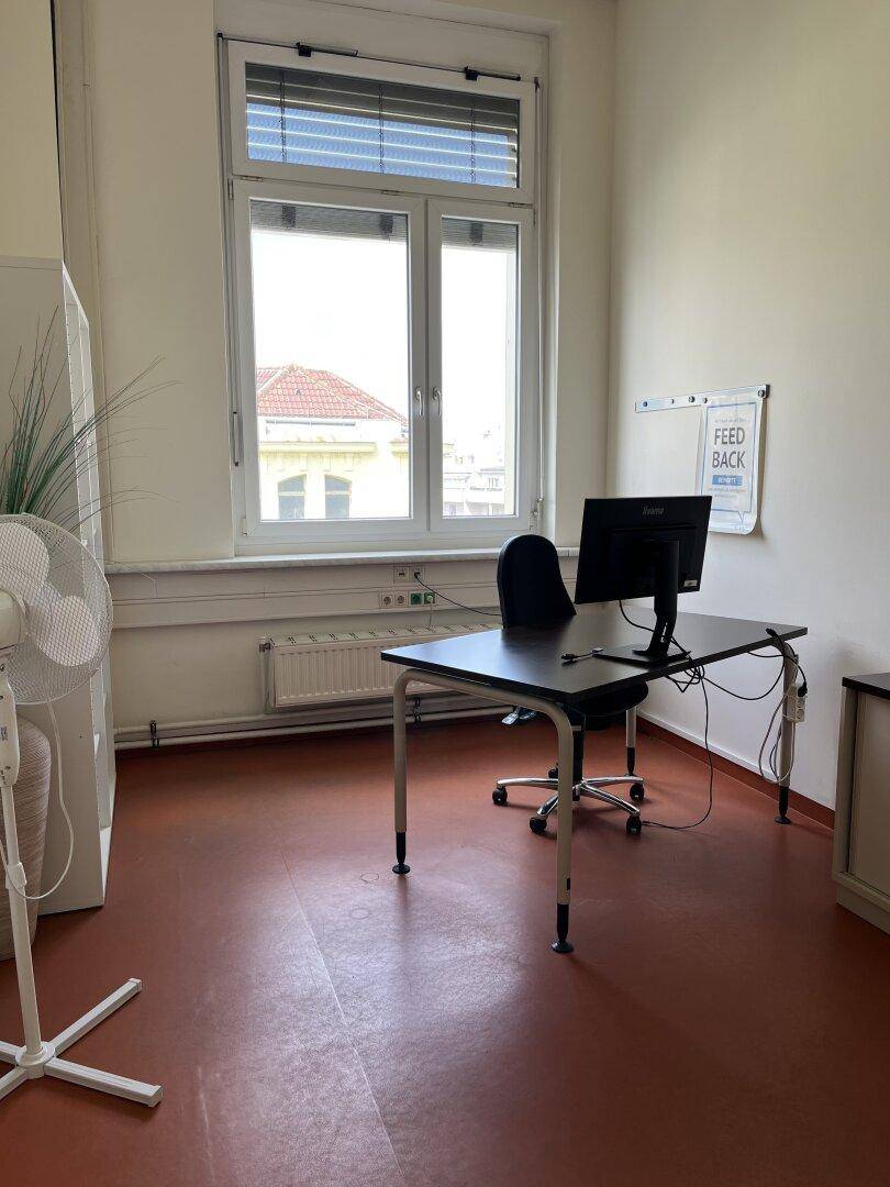 Helles Büro mit einem Schreibtisch, Bürostuhl und einem großen Fenster, das viel Tageslicht hereinlässt.