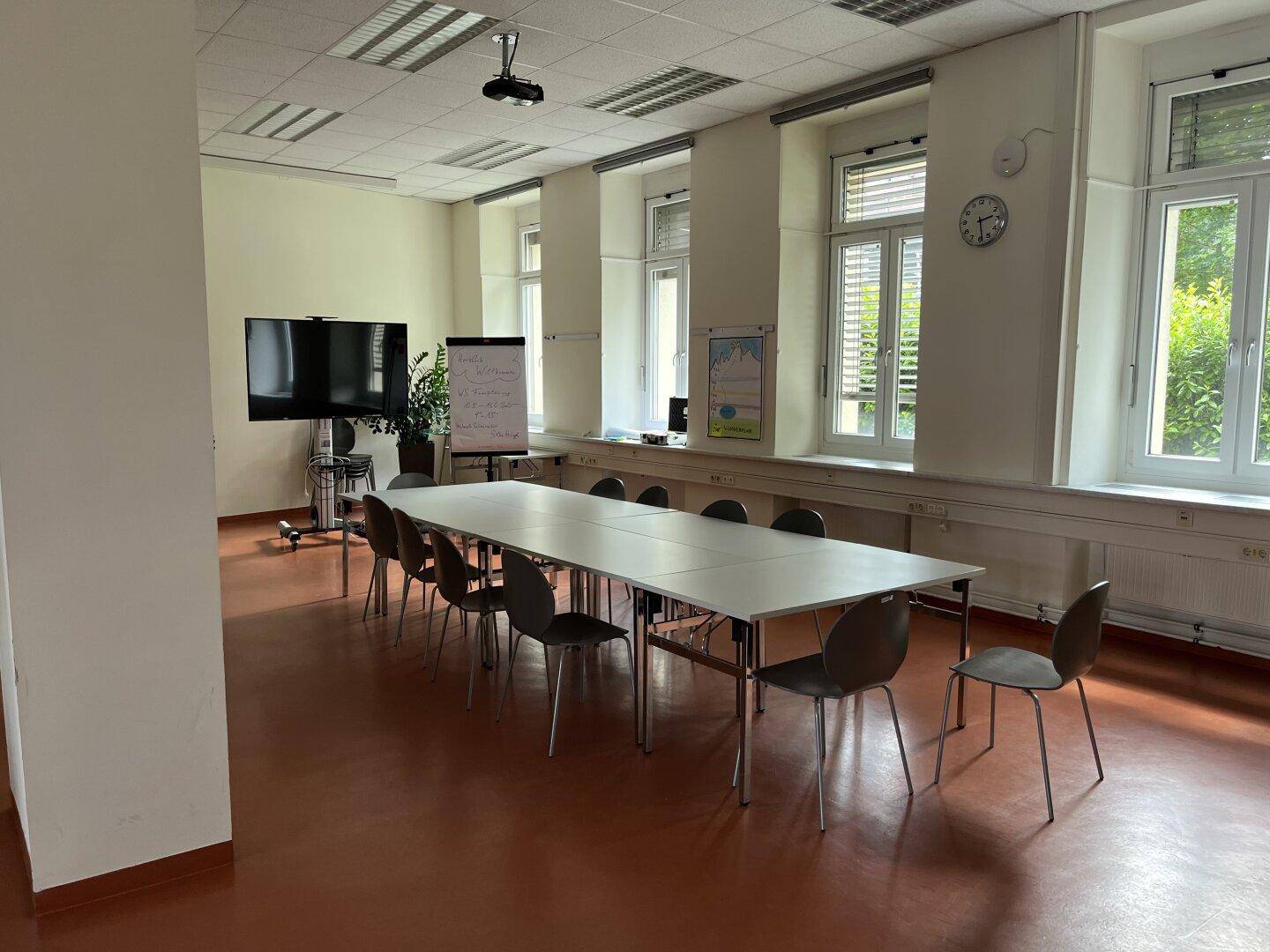 Geräumiger Konferenzraum mit langem Tisch, vielen Stühlen und großen Fenstern für Besprechungen.