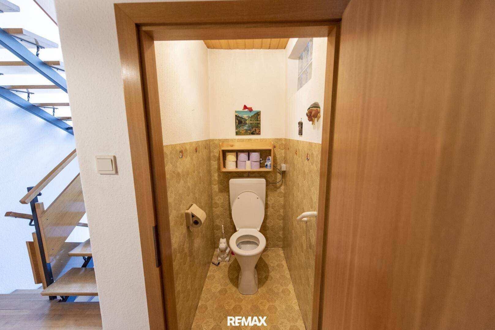 Kleines Gäste-WC mit gemusterter Tapete, Holzdecke und einfacher Toilette.