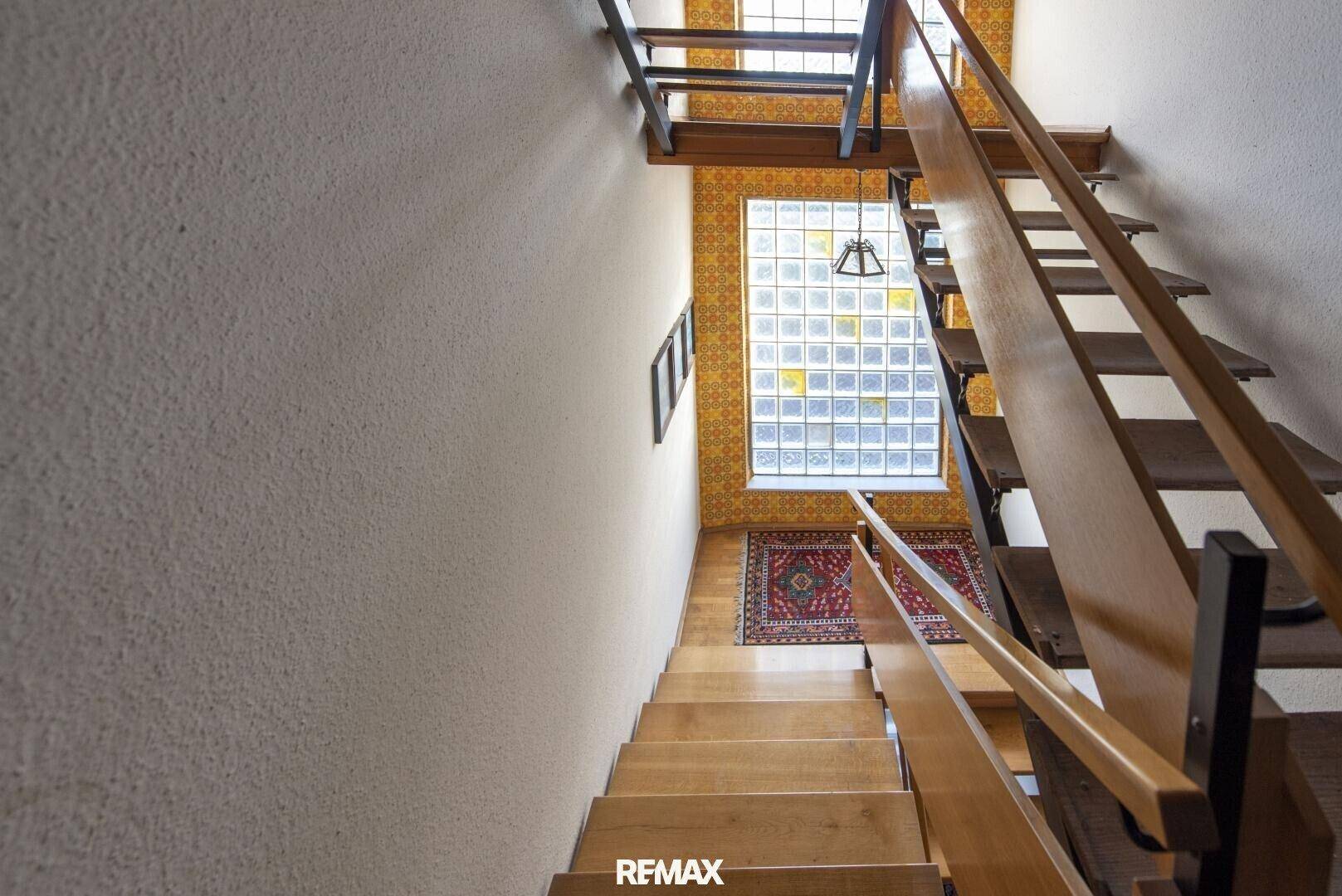 Holztreppe führt nach oben, mit einem großen Glasbausteinfenster, das viel Licht hereinlässt.