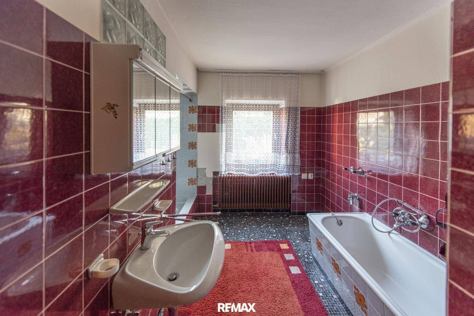 Badezimmer im 80er-Jahre-Stil mit roten Fliesen, Badewanne und einem Fenster für Tageslicht.