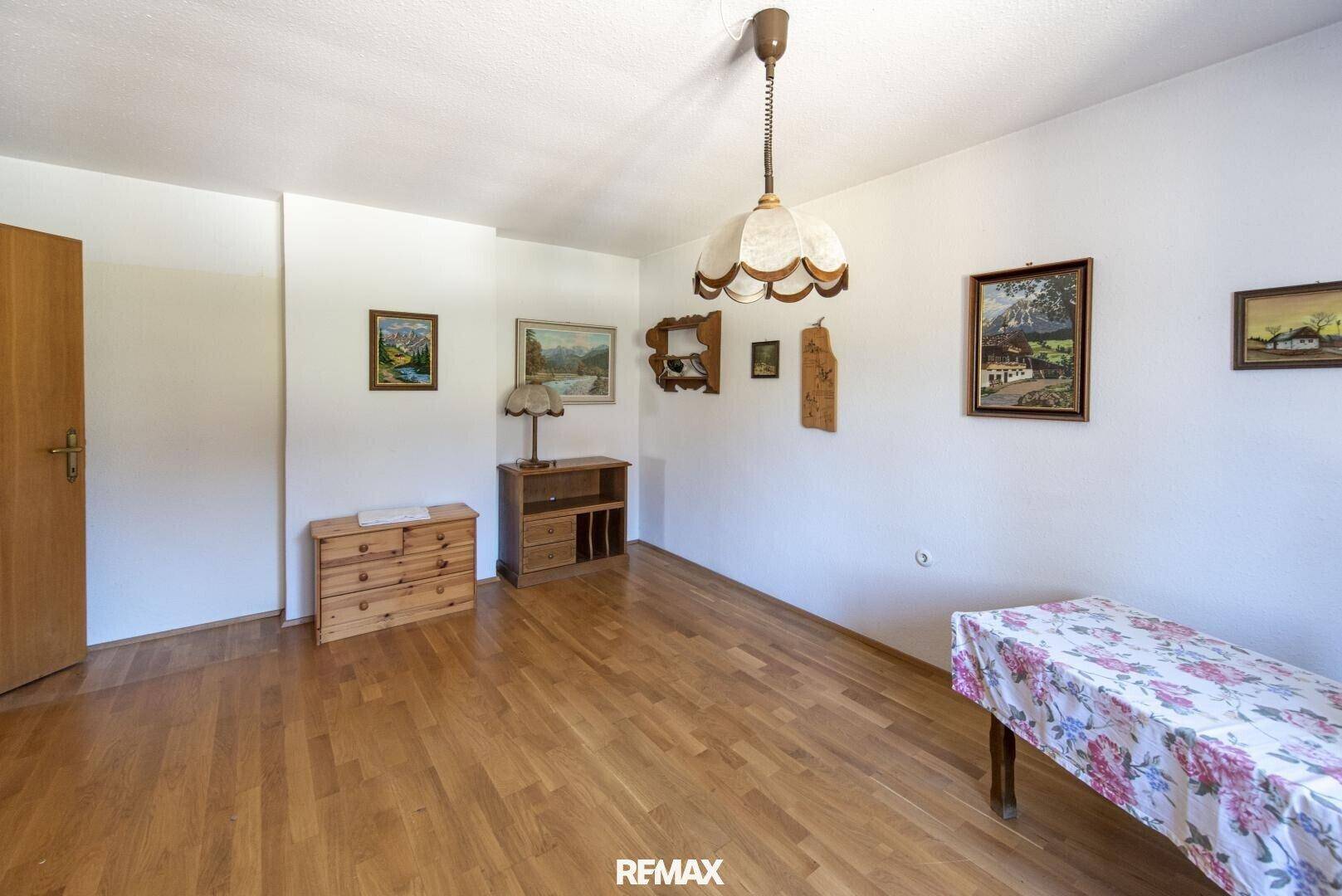 Helles Zimmer mit Holzboden, einfacher Einrichtung und traditionellen Bildern an der Wand.