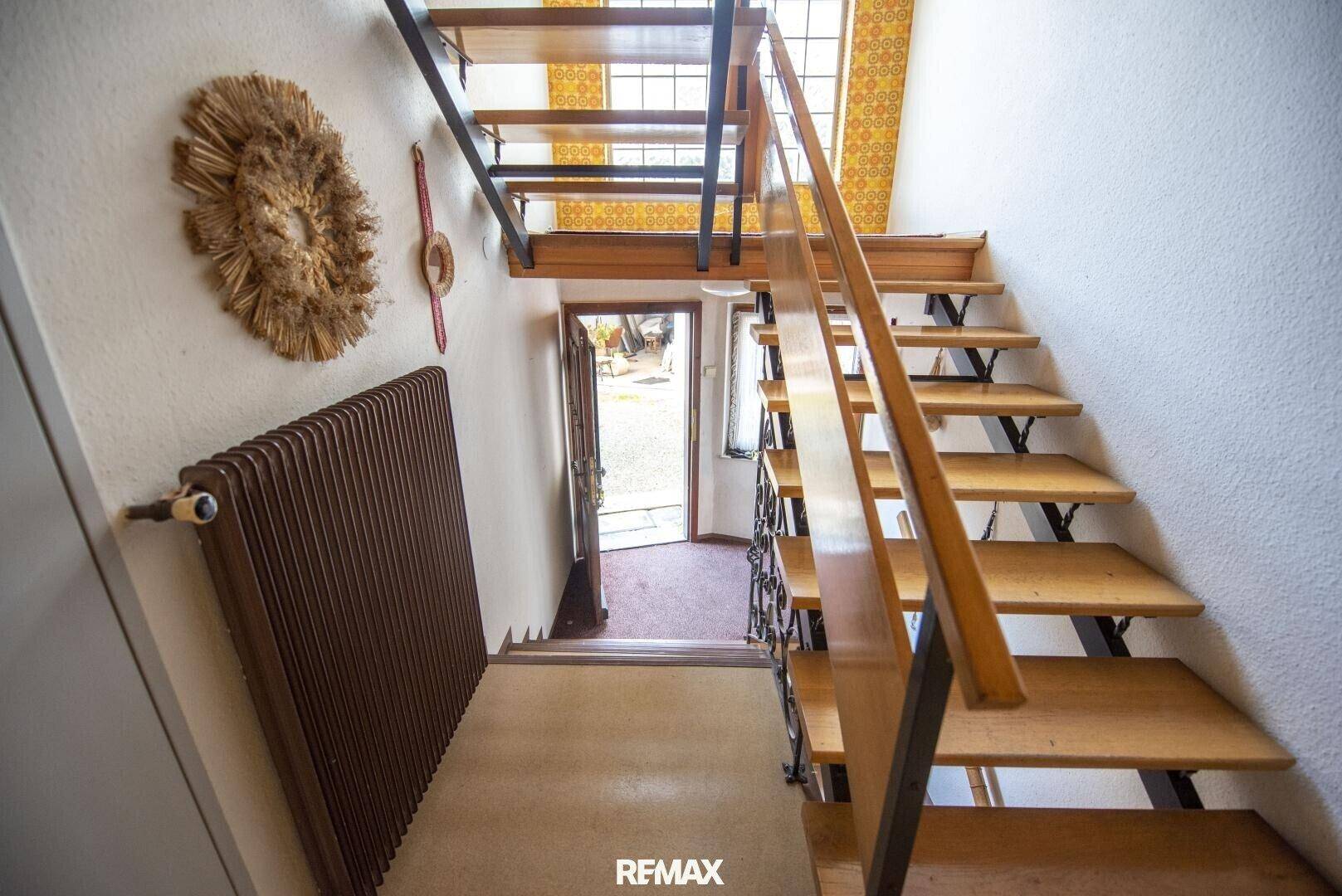 Holztreppe mit Metallgeländer und Heizkörper in einem Flurbereich.