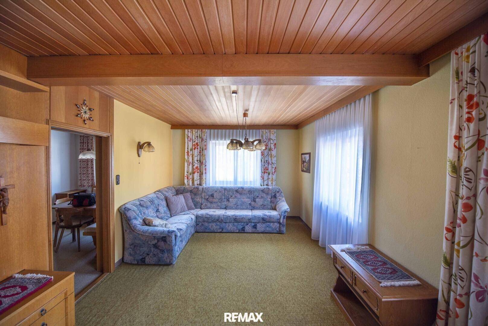Gemütliches Wohnzimmer mit Holzdecke, Teppichboden und floral gemustertem Sofa.