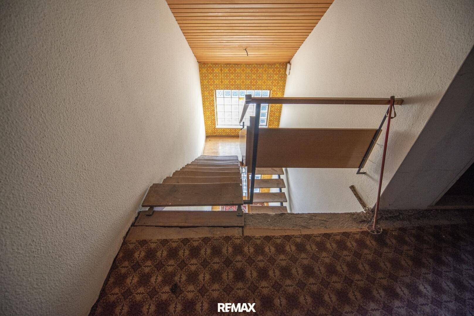 Blick von oben auf eine Holztreppe mit Teppichboden und gemusterter Tapete.