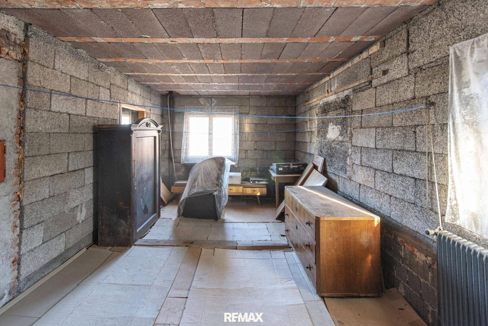 Rohbauzimmer mit Ziegelwänden, Holzbalkendecke und alten Möbelstücken.