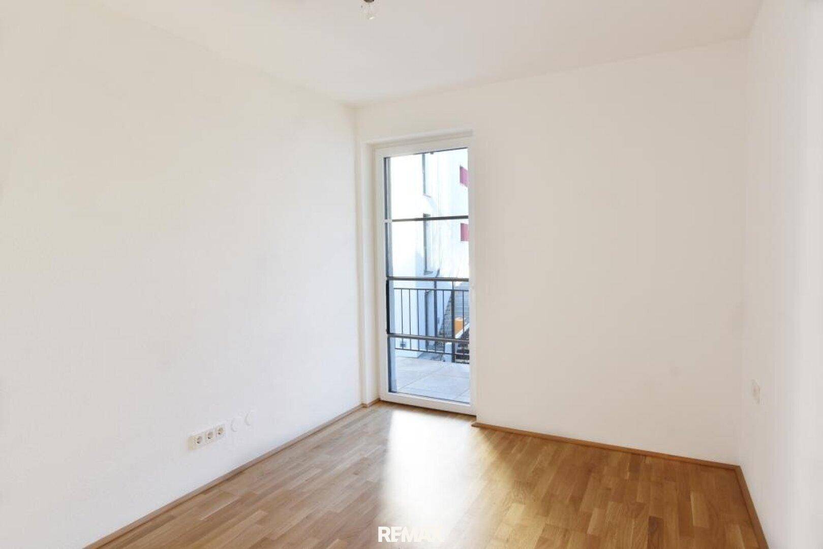 Helles Schlafzimmer mit Holzboden und Zugang zu einem kleinen Balkon oder einer französischen Balkontür.