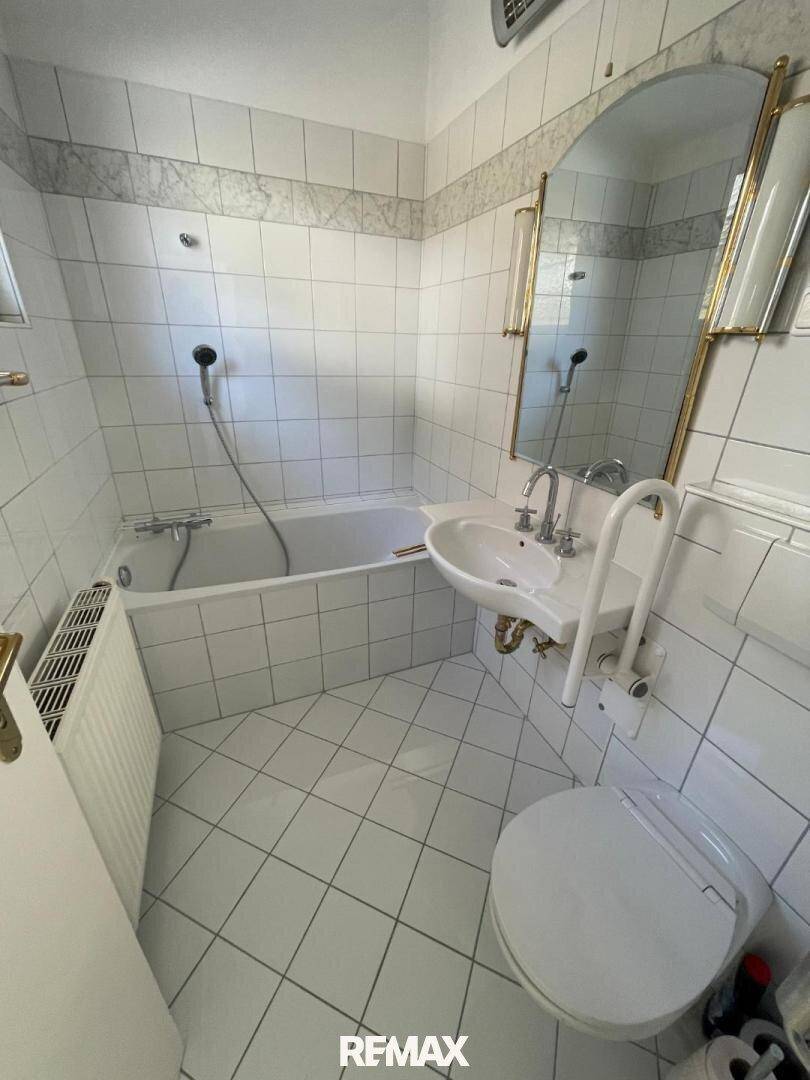Gefliestes Badezimmer mit Badewanne, Waschbecken, Toilette und praktischen Haltegriffen.