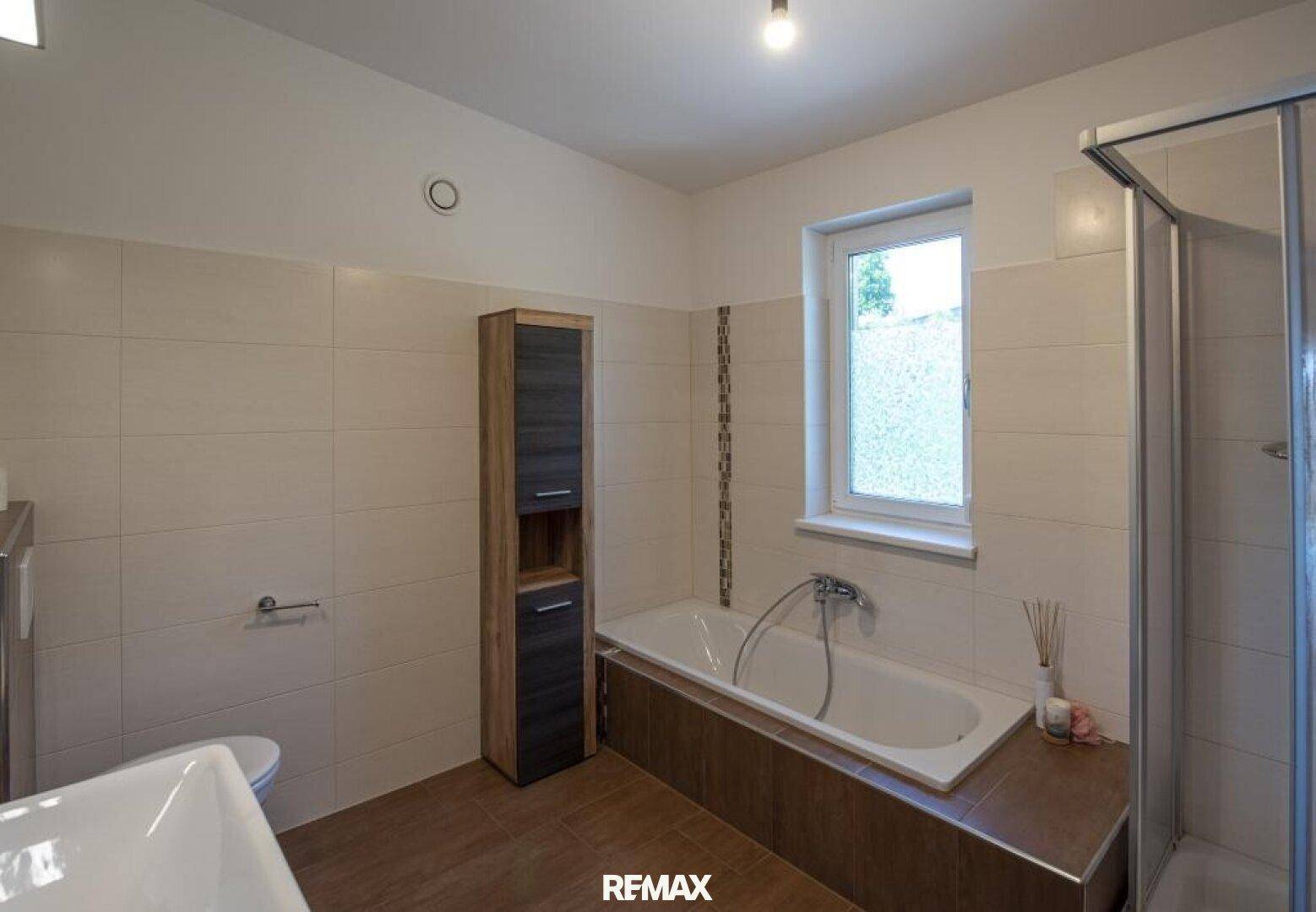 Badezimmer mit beigefarbenen Fliesen, Badewanne, Duschkabine und Fenster.