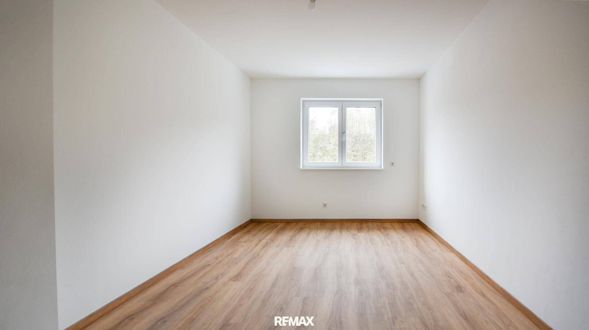 Leerer Raum mit hellem Laminatboden und einem Fenster, das eine angenehme Atmosphäre schafft.