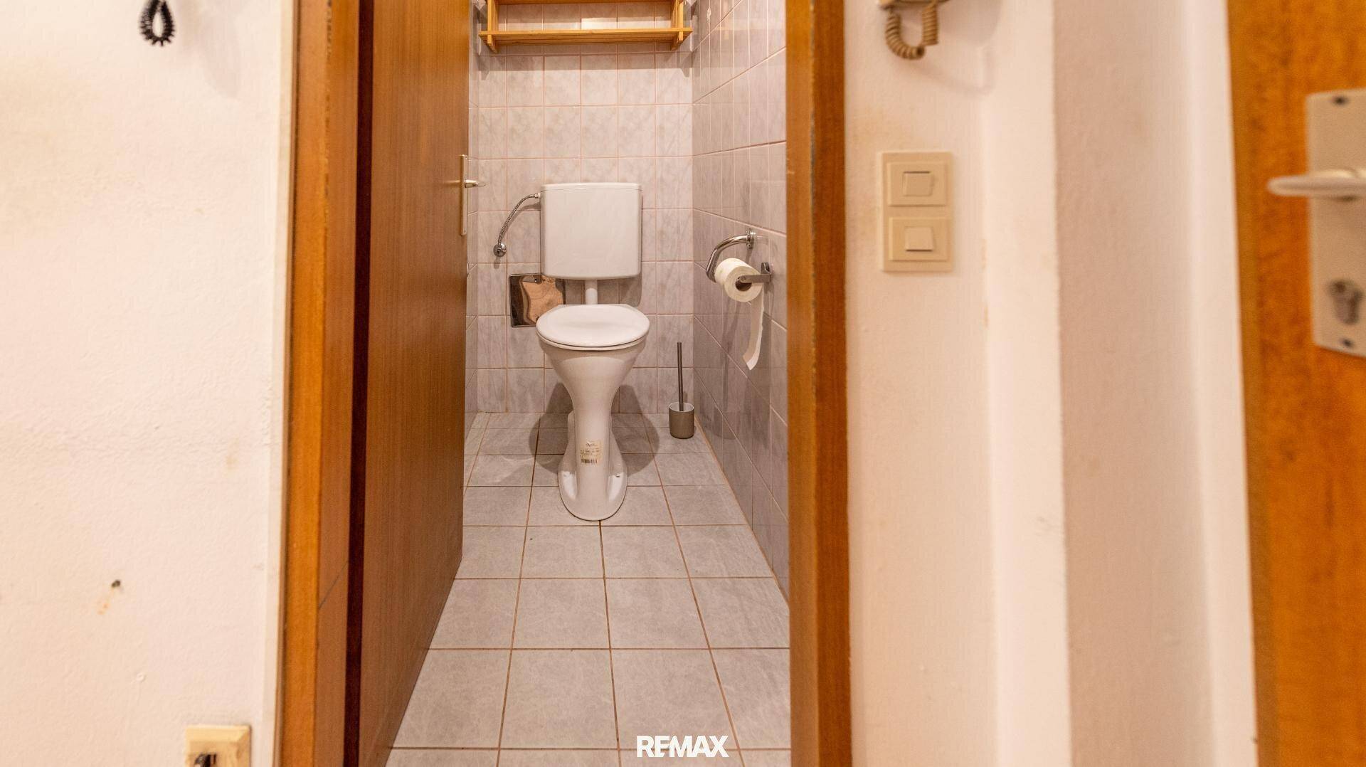 Kleines WC mit weißen Fliesen, Toilette und einfacher Ausstattung.