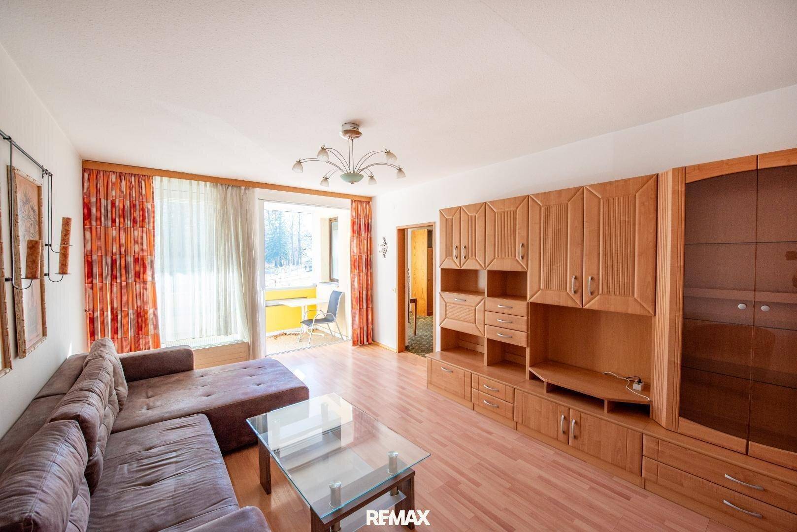 Geräumiges Wohnzimmer mit Holzfußboden, großem Sofa und Zugang zu einem Balkon.