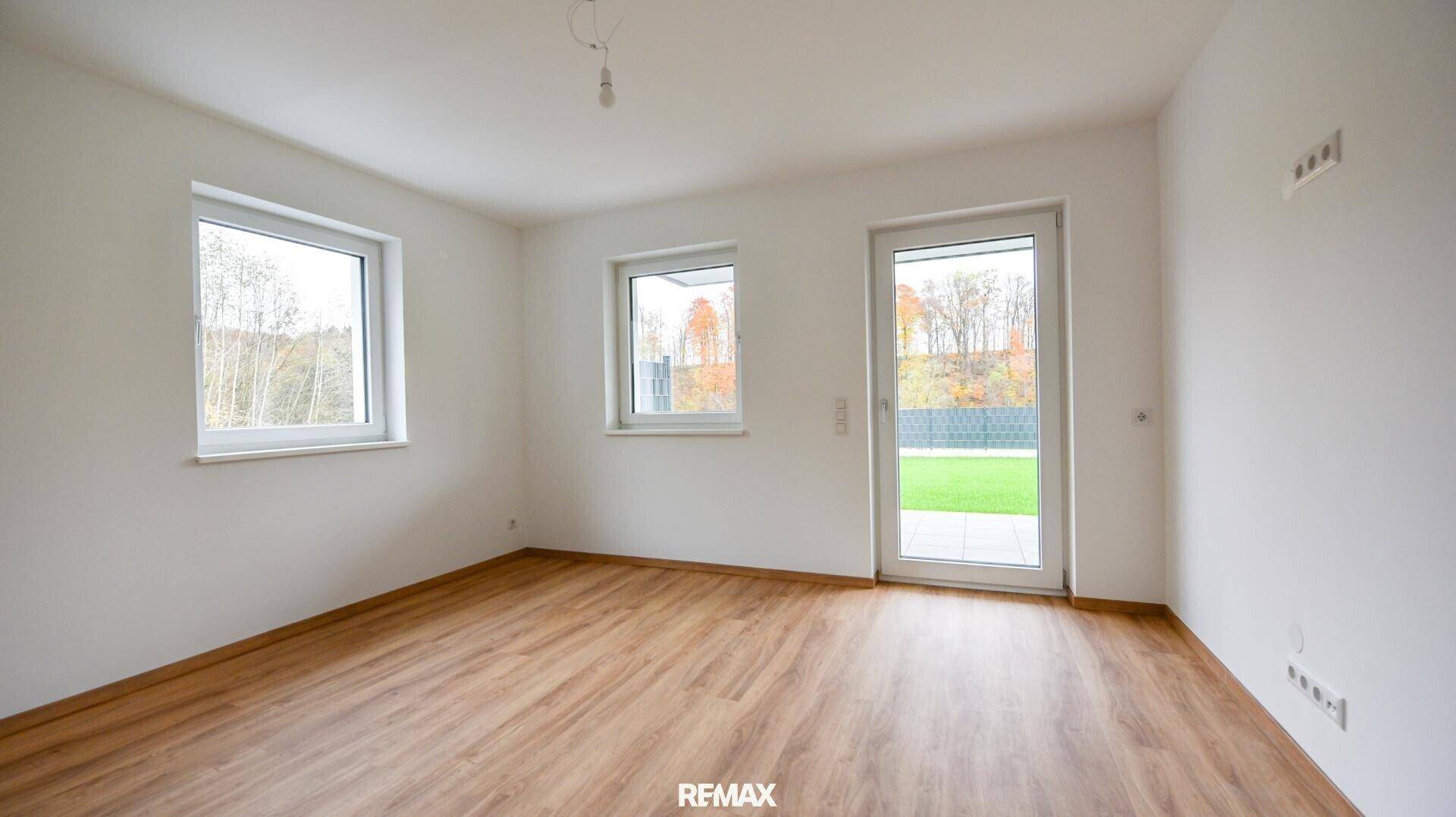 Helles Zimmer mit Holzboden, weißen Wänden und Zugang zu einer Rasenfläche.