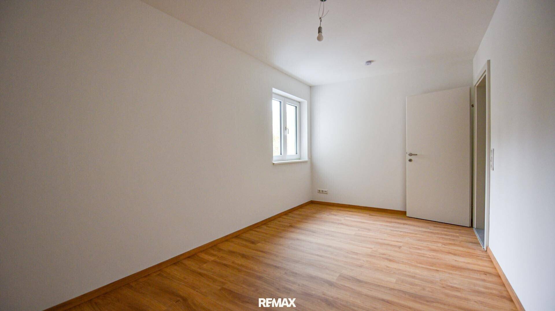 Helles, unmöbliertes Schlafzimmer mit Laminatboden und einem großen Fenster.