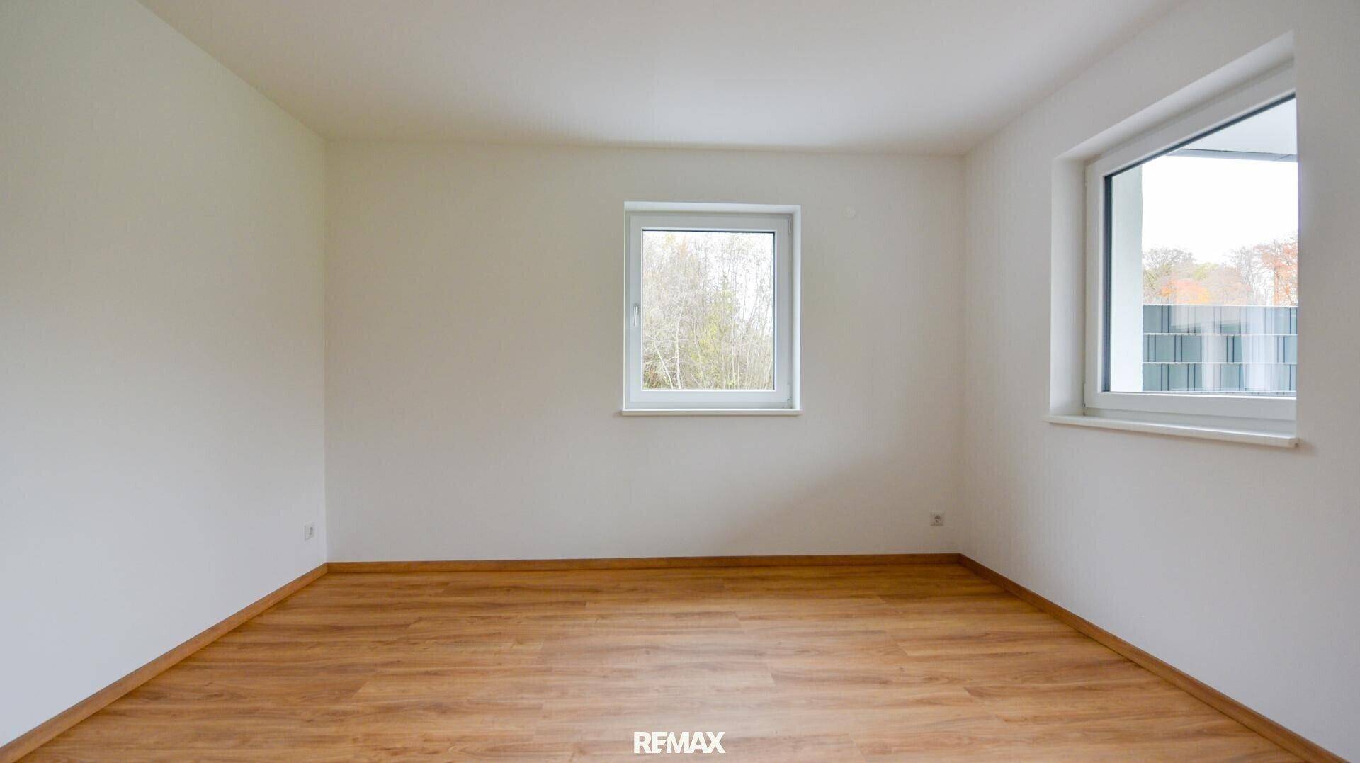 Geräumiges Zimmer mit Holzboden und zwei großen Fenstern für viel Tageslicht.