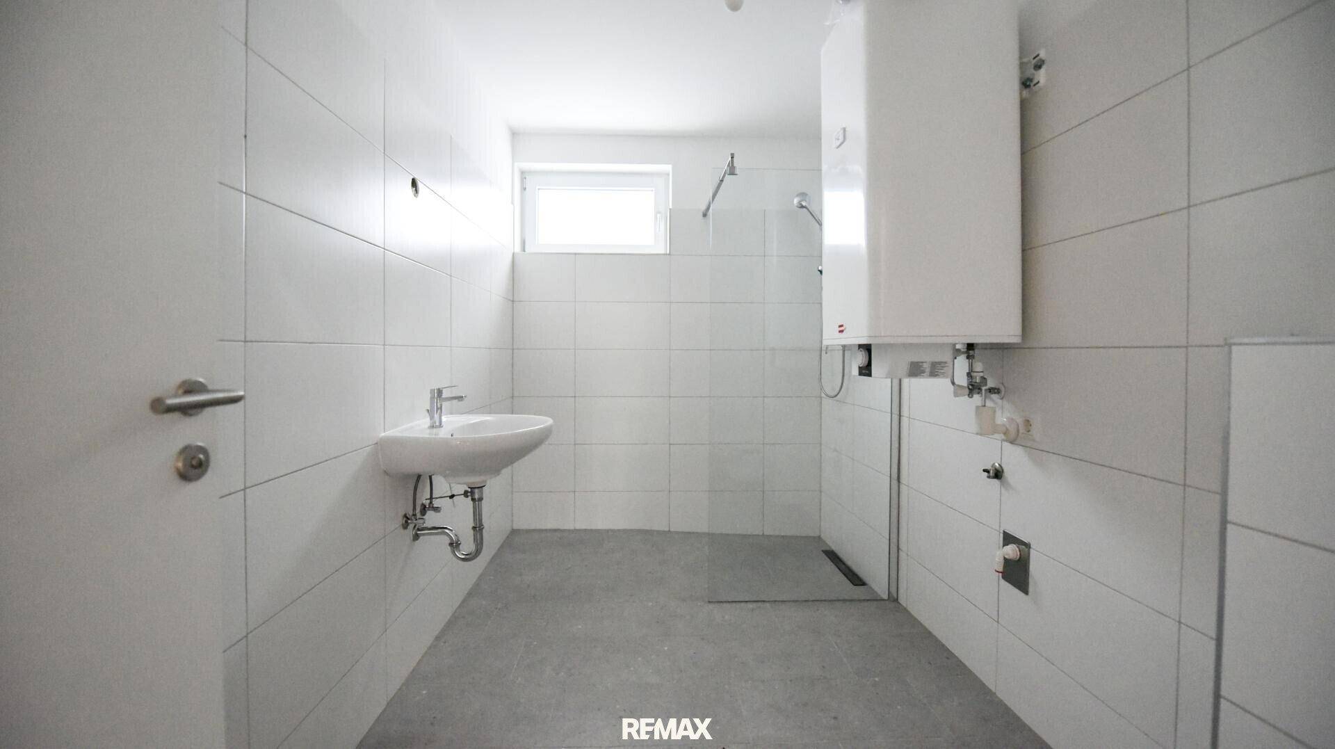 Modern gefliestes Badezimmer mit Waschbecken, Duschbereich und Fenster.