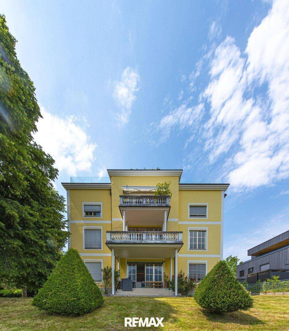 Die gelbe Fassade des Gebäudes mit mehreren Balkonen und großen Fenstern unter blauem Himmel.