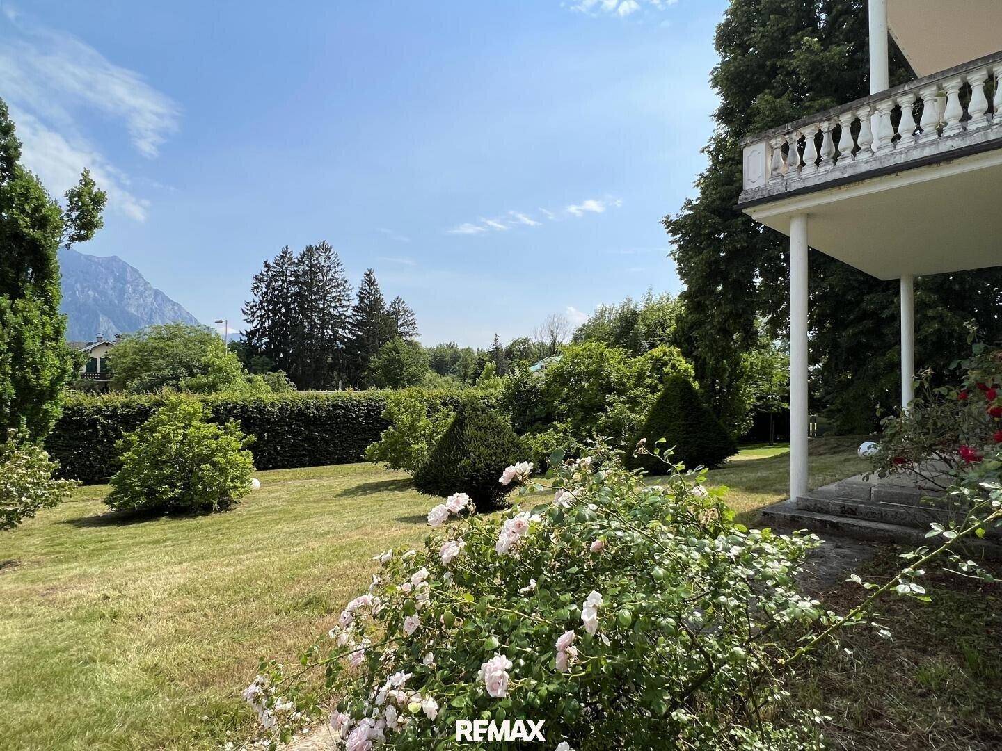 Gepflegter Garten mit Rasenfläche, blühenden Rosen und Blick auf die umliegende Berglandschaft.