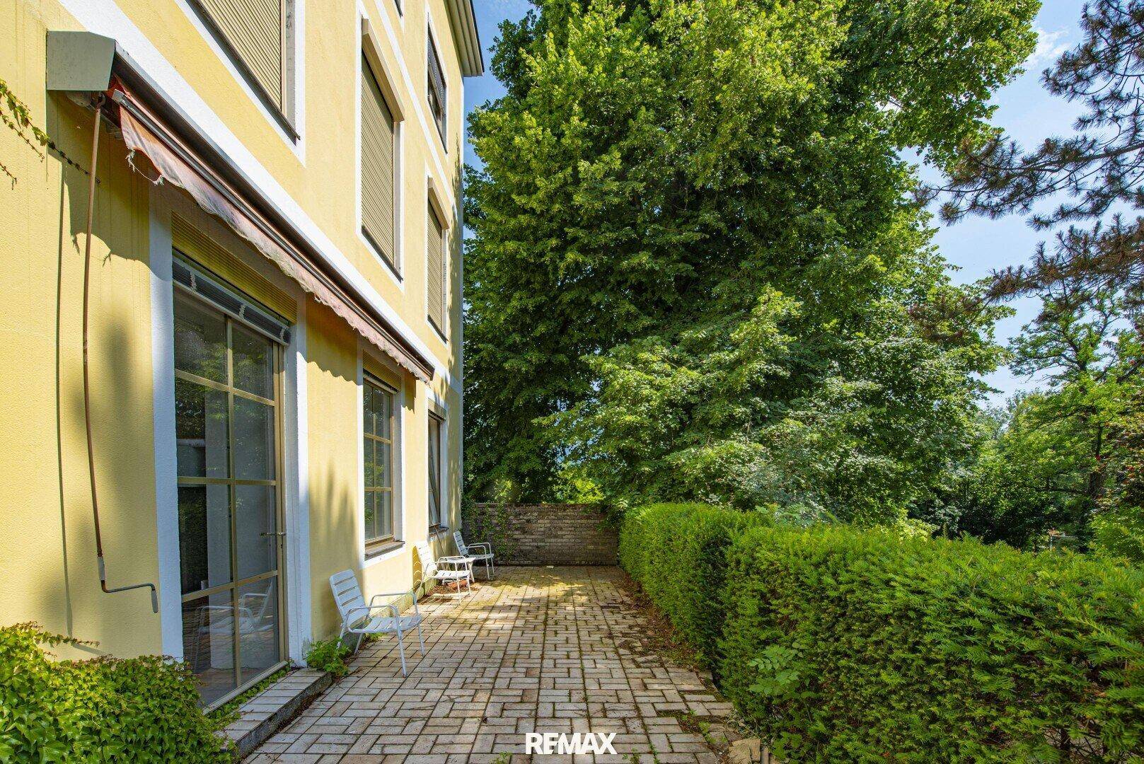 Gepflasterter Terrassenbereich neben dem Gebäude, umgeben von einer grünen Hecke.