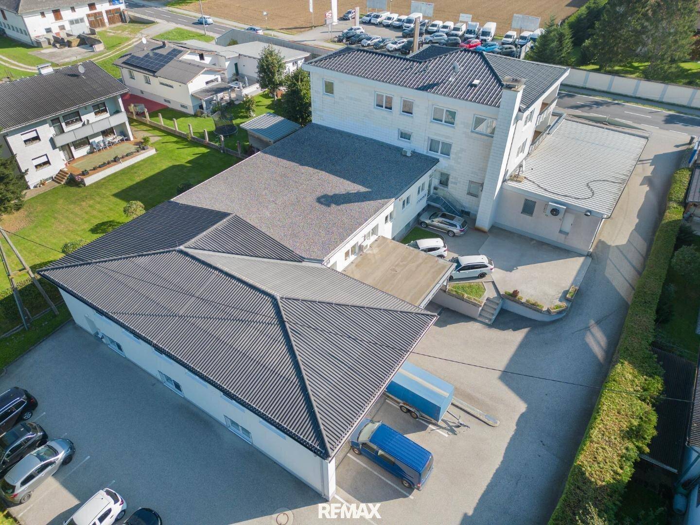 Luftaufnahme eines Gewerbegebäudes mit angrenzendem Parkplatz und umliegender Landschaft.