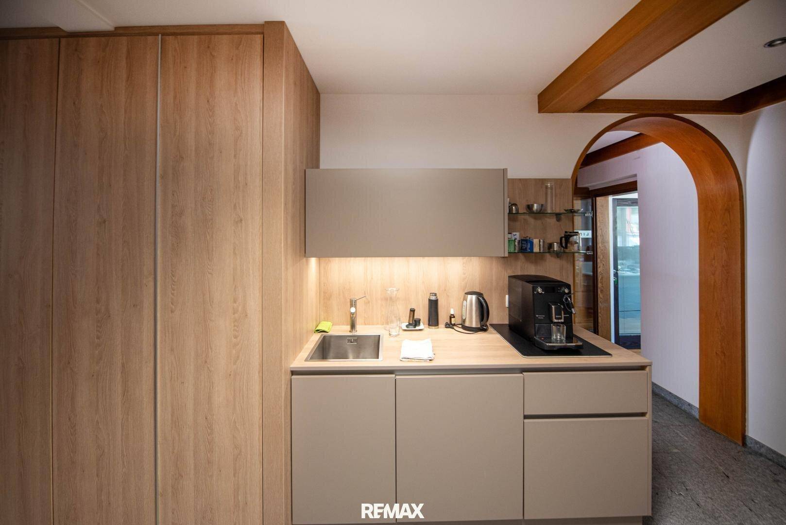 Kompakte Küchenzeile mit Holzschränken, Spüle und Kaffeemaschine, in einem modernen Design.