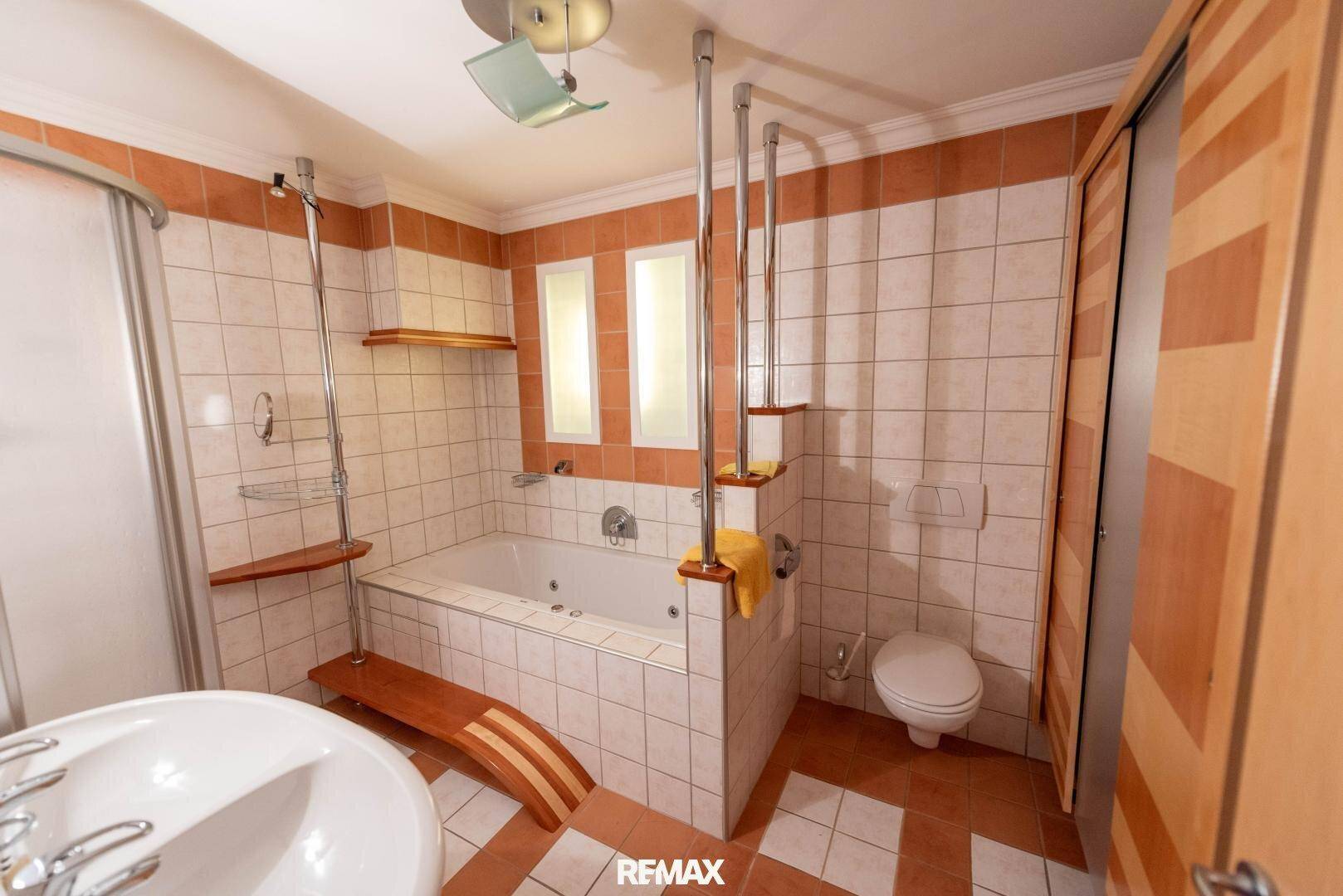 Gefliestes Badezimmer mit Badewanne, separater Duschkabine und Toilette in warmen Farbtönen.