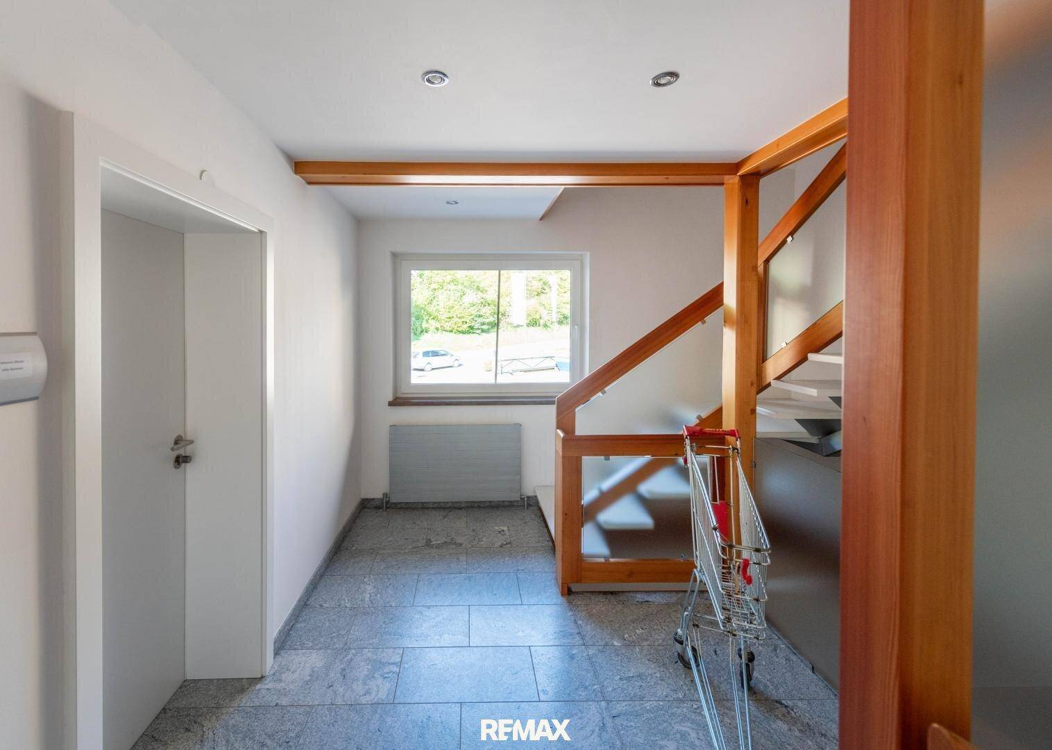 Heller Eingangsbereich mit Holztreppe, gefliestem Boden und einem Fenster, das Tageslicht hereinlässt.