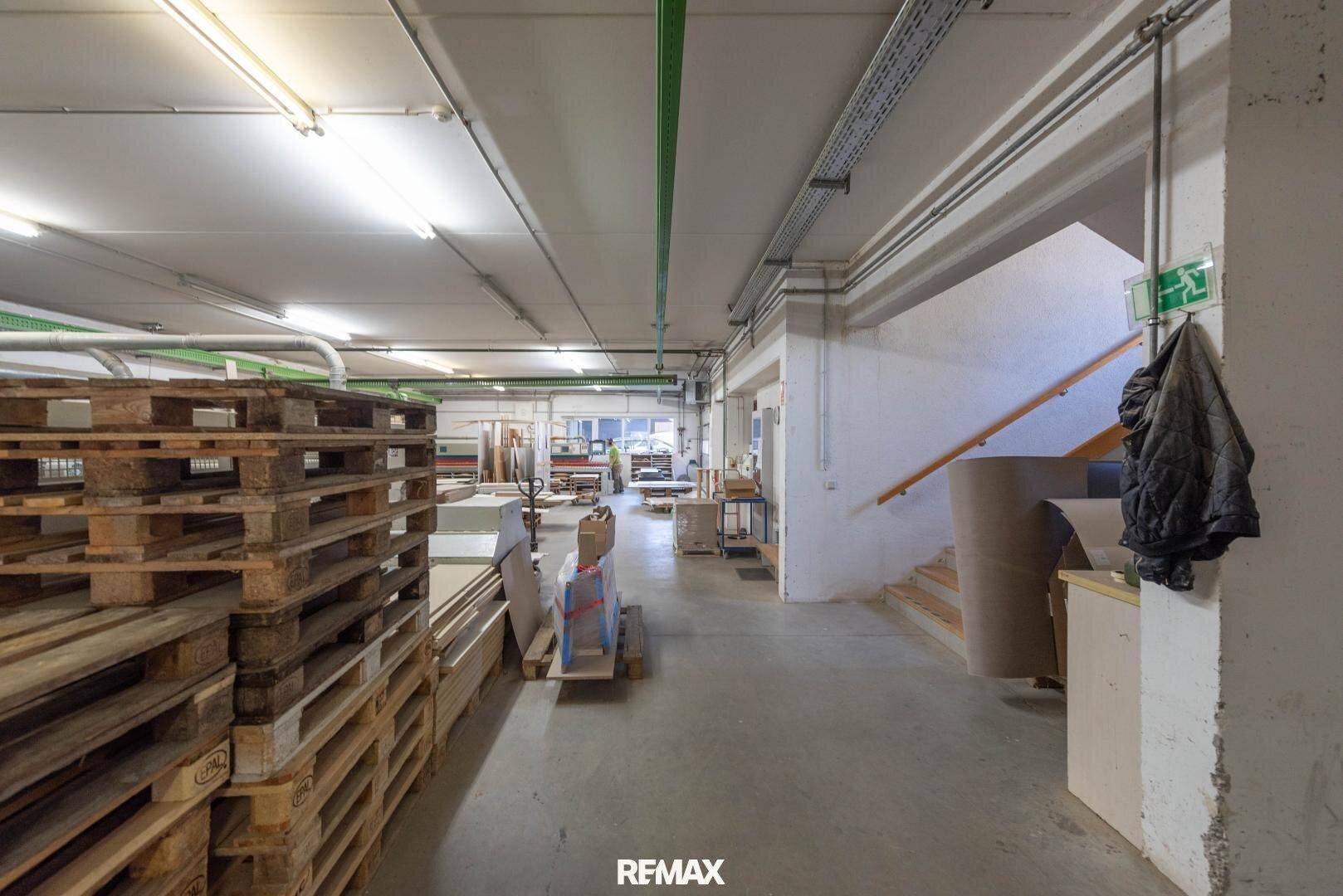 Innenansicht einer Lagerhalle mit Holzpaletten, einer Treppe und einem Notausgangsschild.
