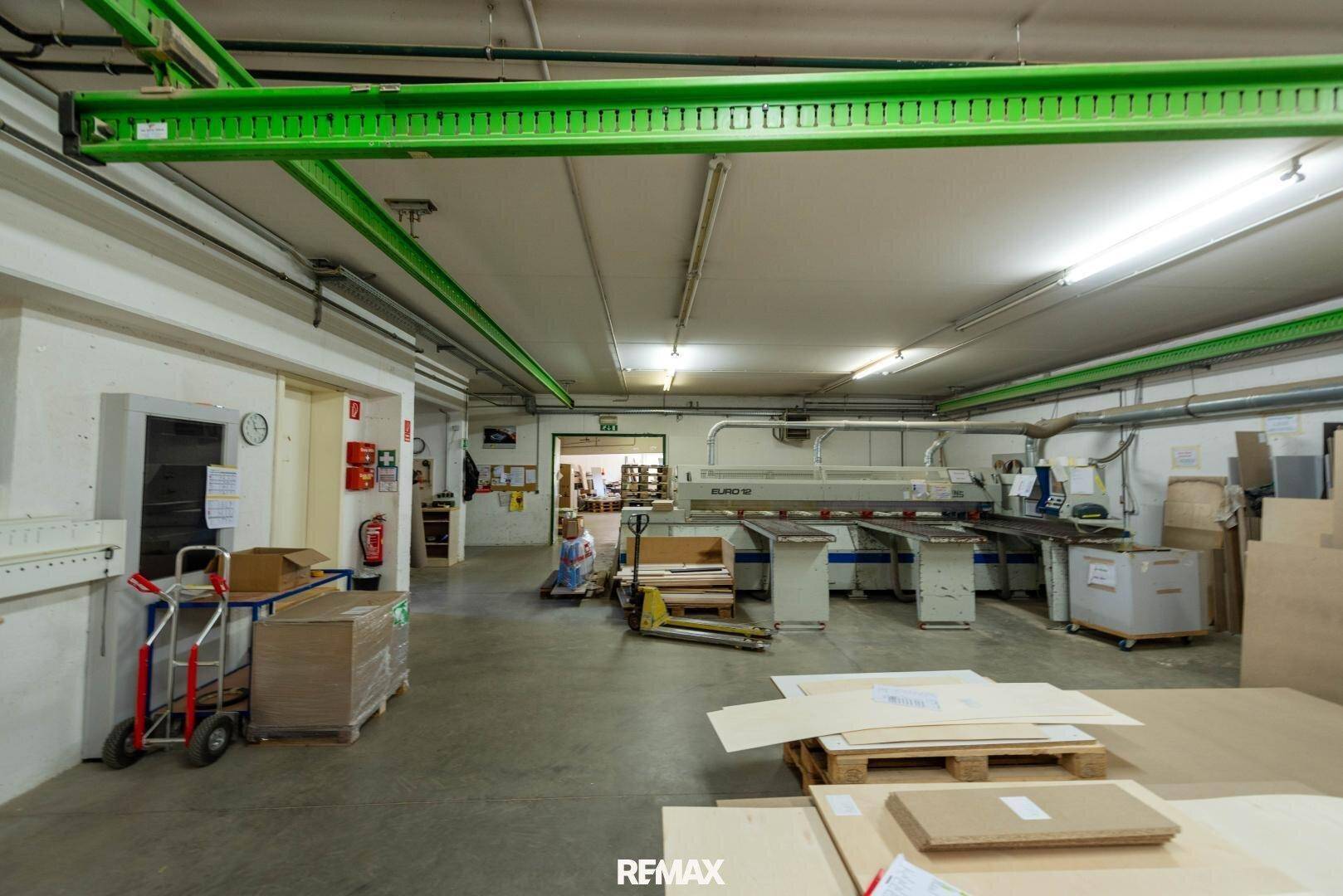 Geräumige Werkstatt oder Produktionshalle mit Holzbearbeitungsmaschinen und gestapelten Materialien.