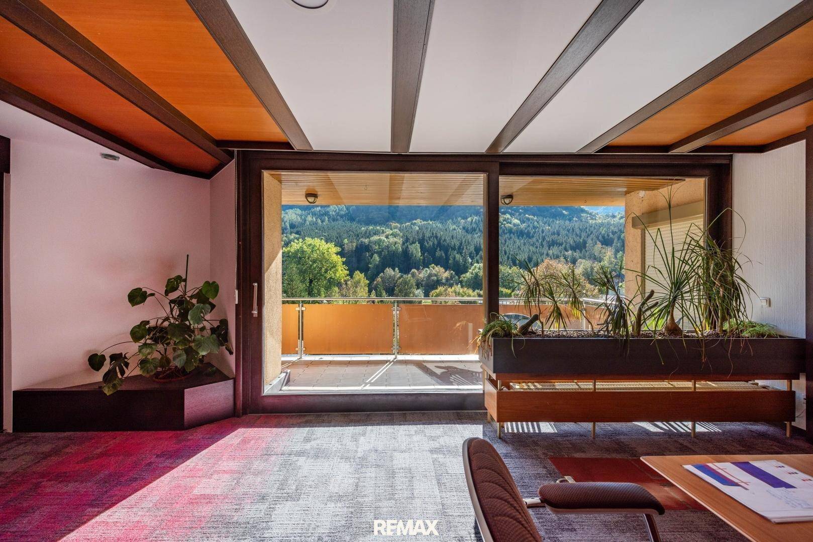 Büro mit großen Fenstern, die einen weiten Blick auf die Berge und die grüne Landschaft bieten.