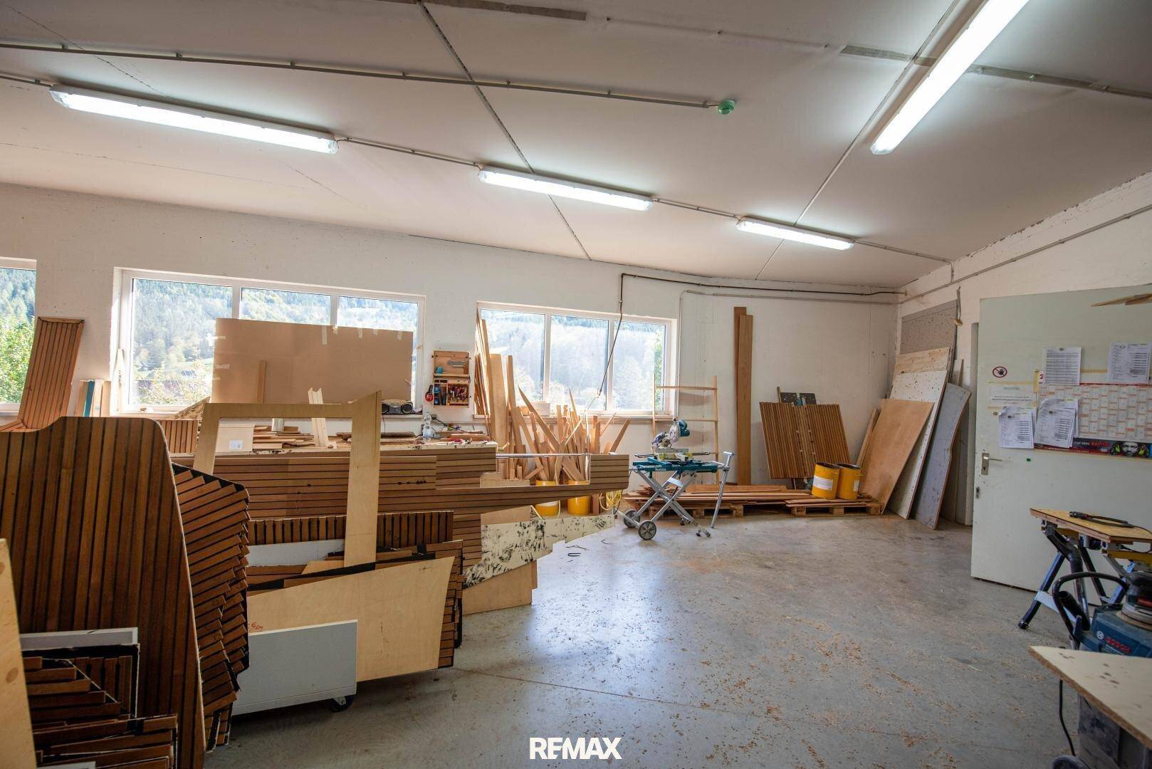 Helle Werkstatt mit zahlreichen Holzstücken, Werkzeugen und Fenstern mit Blick ins Grüne.