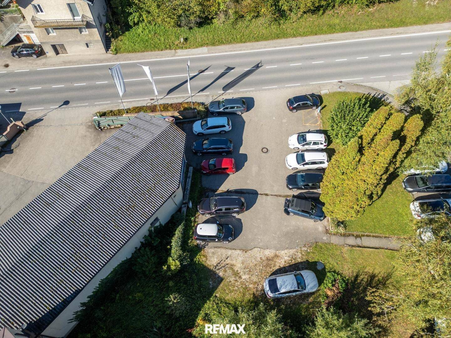 Luftaufnahme eines Parkplatzes neben einer Straße und einem Gebäude mit grüner Umgebung.