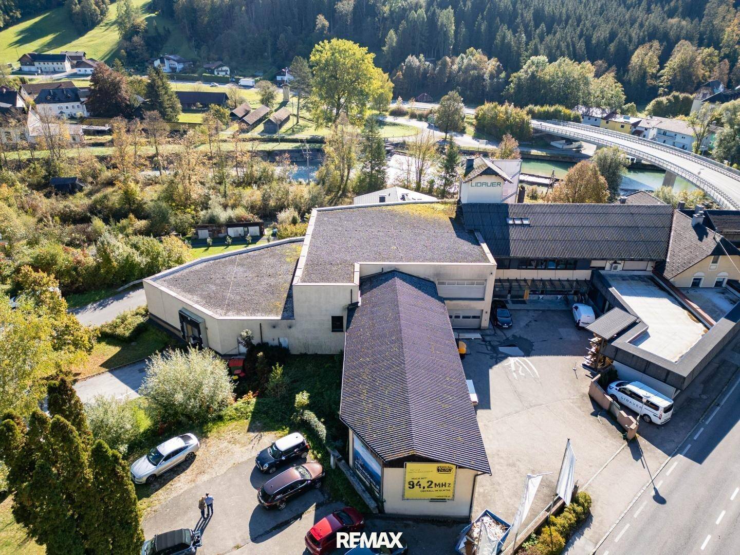 Luftaufnahme des Gebäudekomplexes mit umliegender Natur, einem Fluss und einer Brücke im Hintergrund.