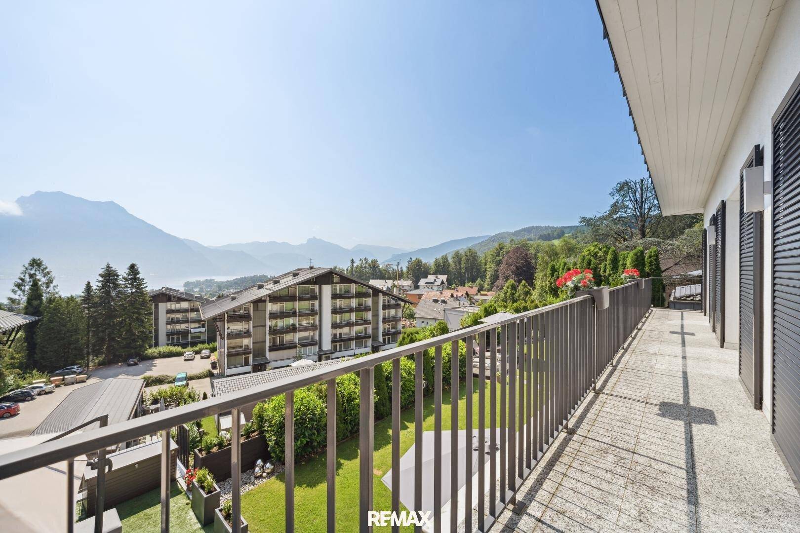 Langer Balkon mit Panoramablick auf die Berge und den See, umgeben von grüner Landschaft.