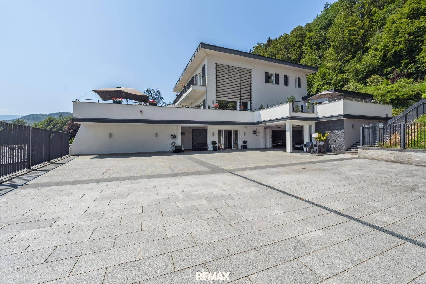 Moderne Villa mit weitläufiger gepflasterter Auffahrt und Terrassenbereichen im Grünen.